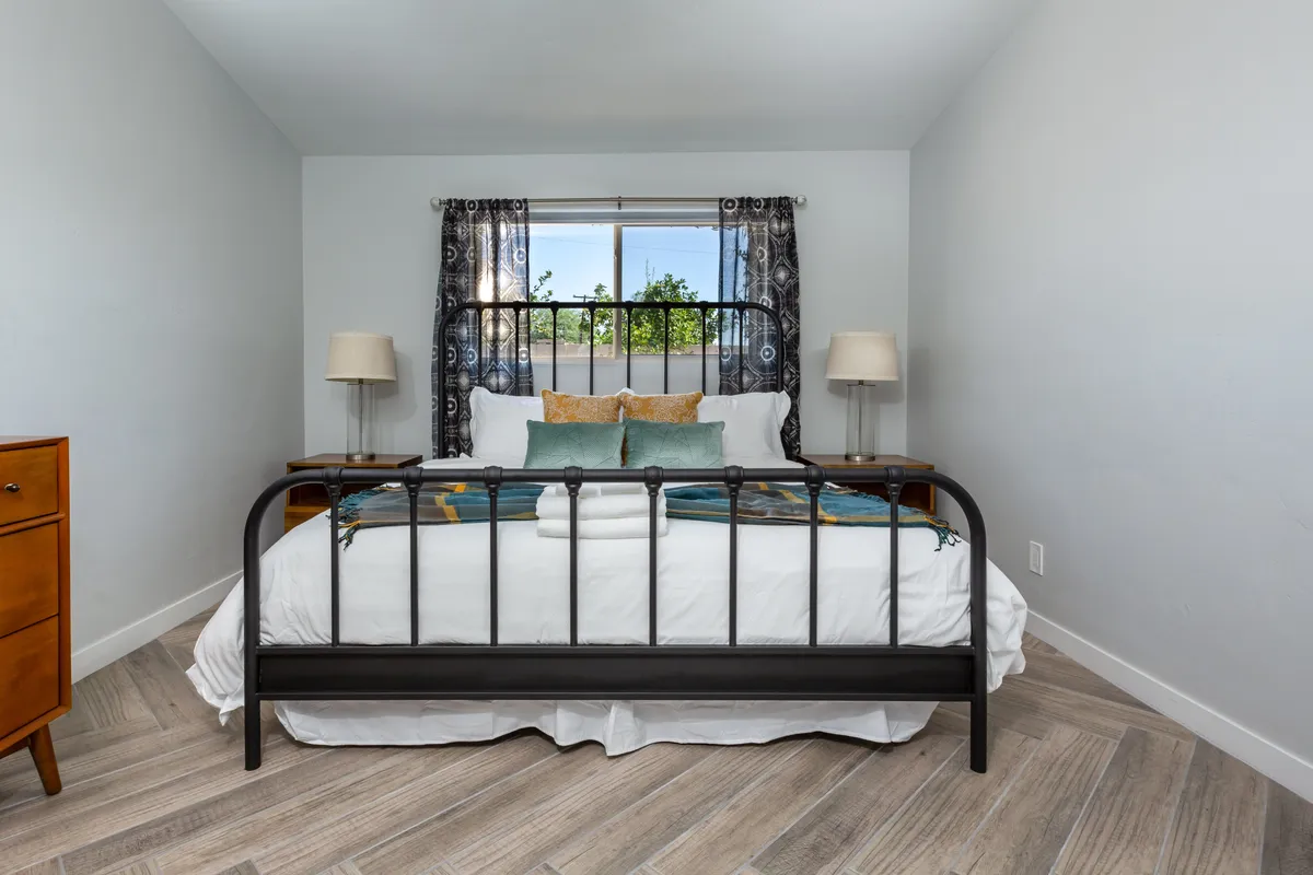 A cozy bedroom with a plush bed topped with decorative pillows, soft lighting, nightstands on each side, and a window letting in gentle natural light. The ambiance is peaceful and inviting, ideal for winding down after a long day.