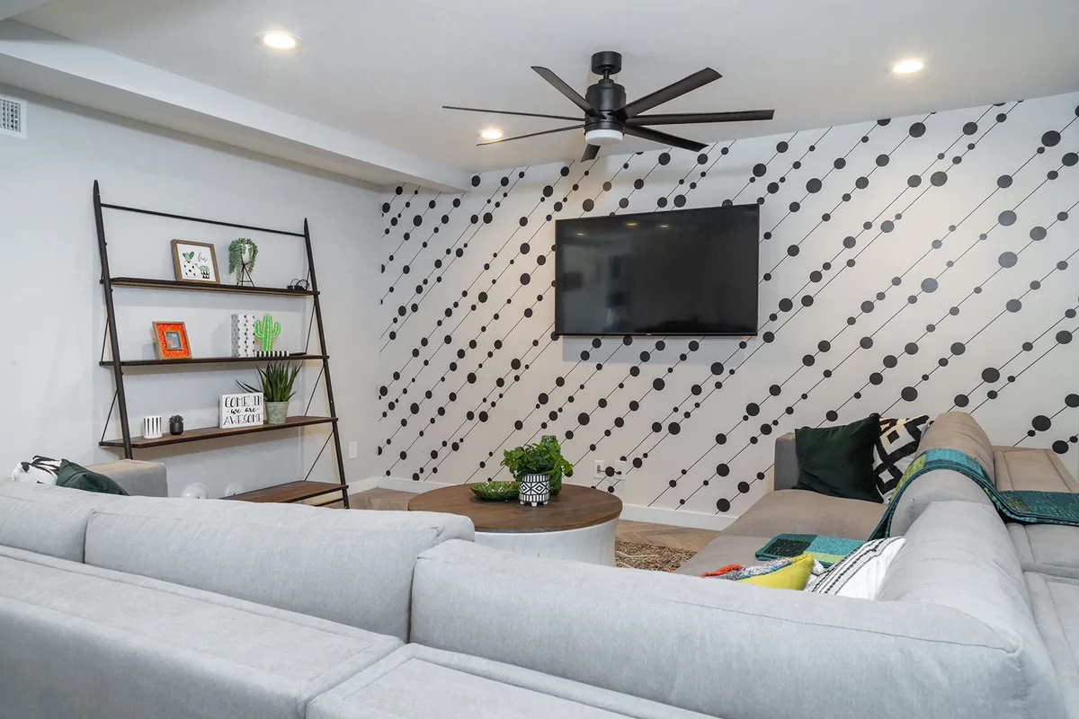 A modern living room with a plush sofa, decorative wall accents, a large TV mounted on the wall, and stylish shelving with curated decor. The setup invites guests to enjoy cozy movie nights or casual conversations.