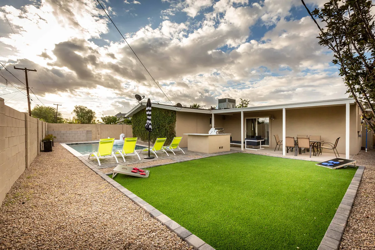 This exterior image captures a spacious backyard featuring a swimming pool, a well-manicured lawn, comfortable outdoor seating, and a barbecue area. The setting is perfect for relaxation and social gatherings, with plenty of room for lounging, swimming, and grilling.