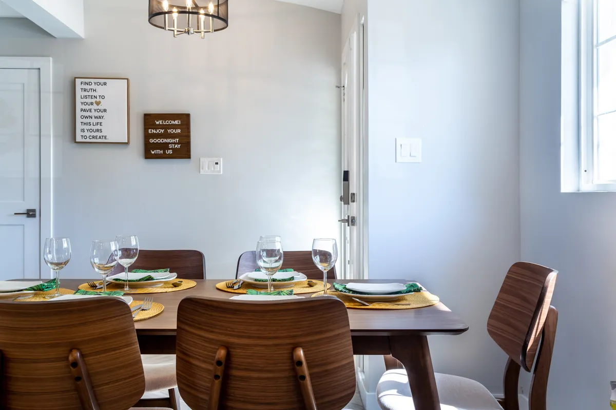This image focuses on the dining table surrounded by comfortable chairs and illuminated by an attractive lighting fixture. Decorative wall signs add a touch of personality, and the mood is set for intimate dinners or lively group celebrations.