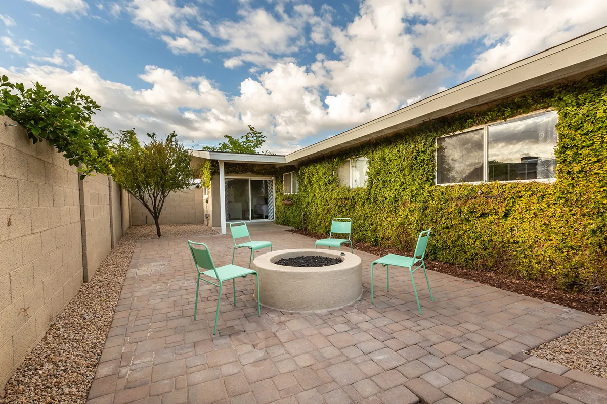 A cozy fire pit is surrounded by green chairs and framed by a lush ivy wall, creating an intimate setting for evening gatherings and stargazing. The mood is casual, cheerful, and perfect for winding down the day.