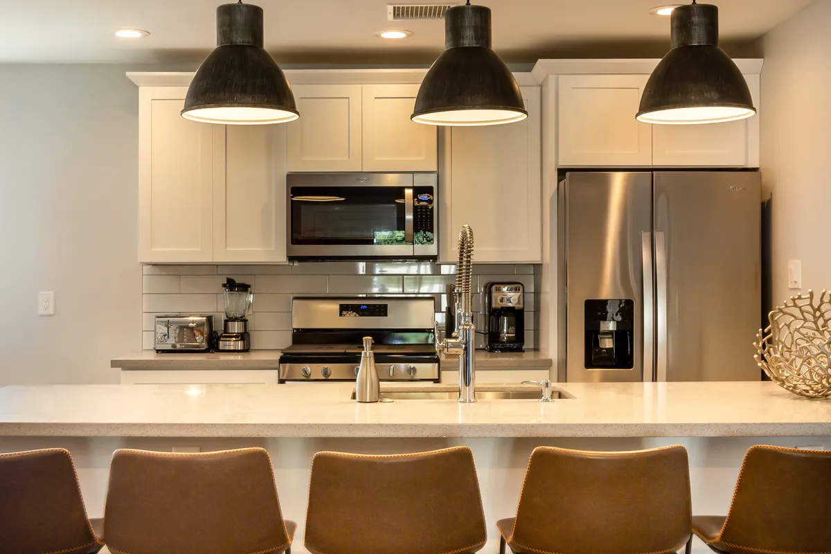 An open kitchen with a central island, pendant lighting, stainless steel appliances, and bar stools for casual gatherings. The layout flows seamlessly into adjoining spaces, ideal for socializing and convenient access during group activities.