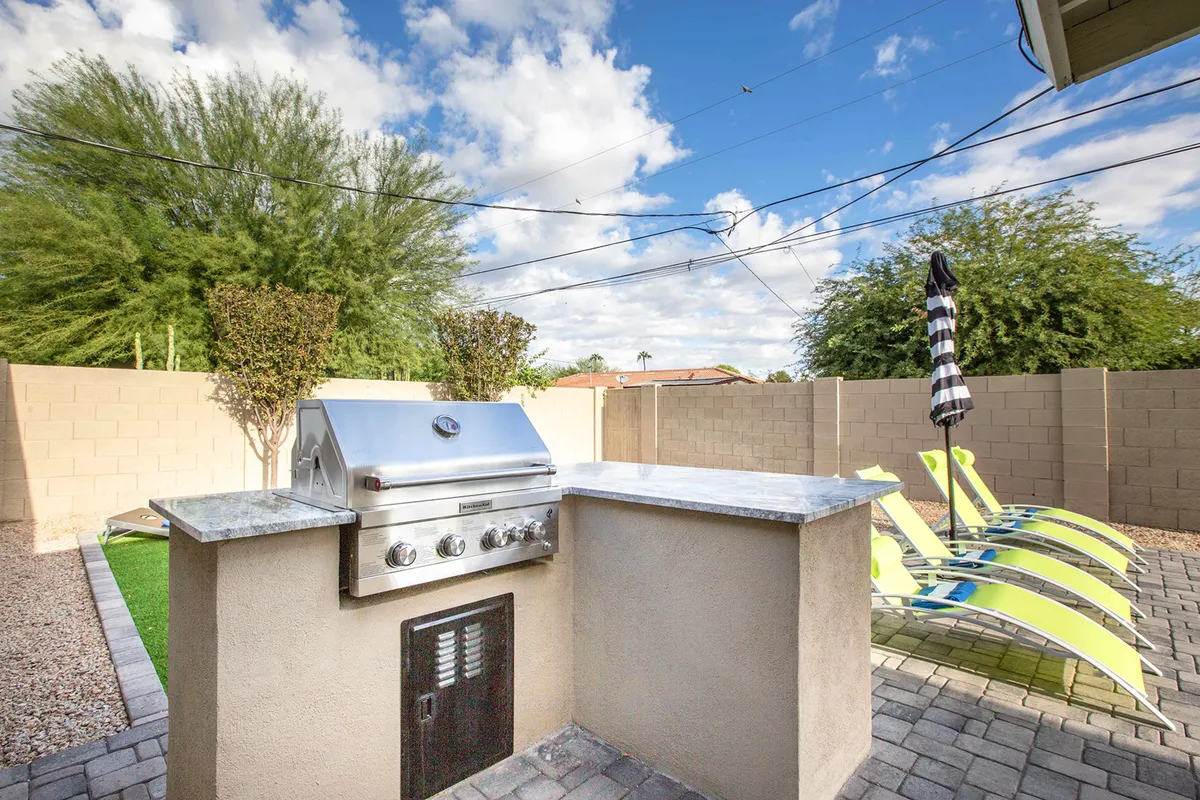 This exterior shot spotlights a modern grill and BBQ area, flanked by lounge chairs and lush landscaping. The scene exudes a laid-back yet inviting atmosphere ideal for al fresco dining and outdoor feasts.